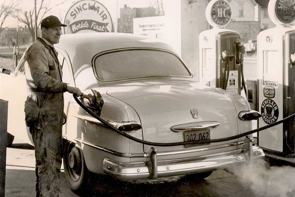 Black & white photo from 1950's of a gas station attendant pumping gas at a Sinclair station
