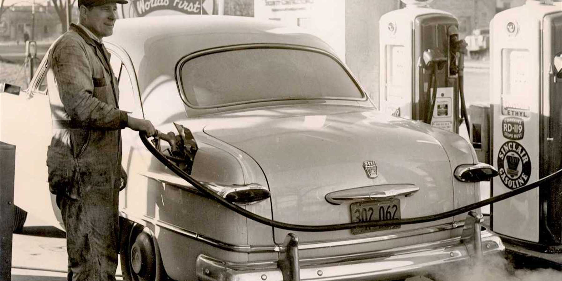 Black & white photo from 1950's of a gas station attendant pumping gas at a Sinclair station