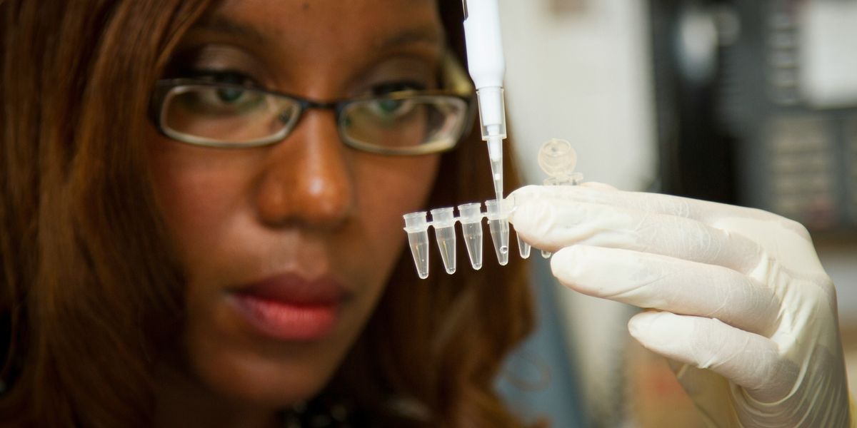 Black woman scientist wearing gloves and glasses injects a liquid into tiny test tubes.