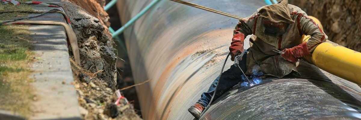 Blue-jean clad worker in heavy coat and gloves welding pipeline