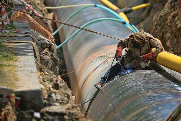 Blue-jean clad worker in heavy coat and gloves welding pipeline