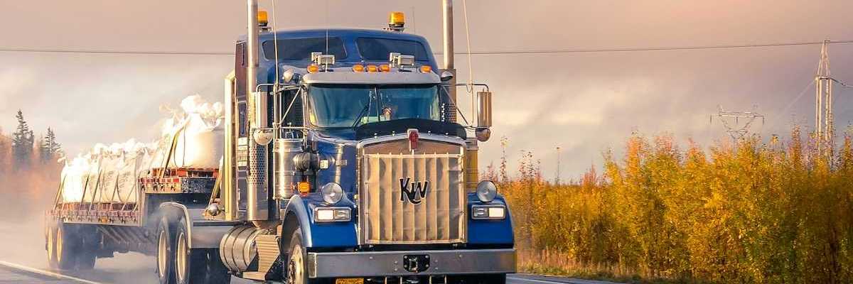 Blue semi truck pulling a flatbed trailer on a two lane highway
