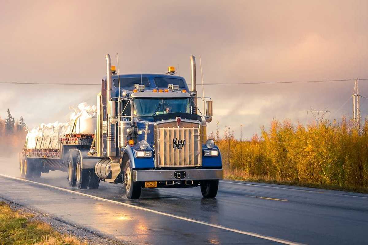 Blue semi truck pulling a flatbed trailer on a two lane highway