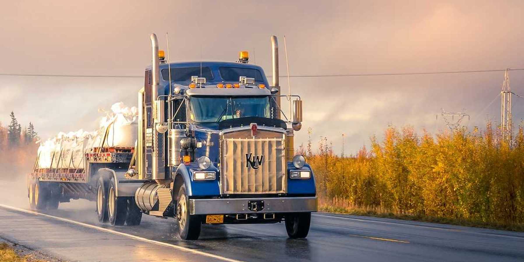 Blue semi truck pulling a flatbed trailer on a two lane highway