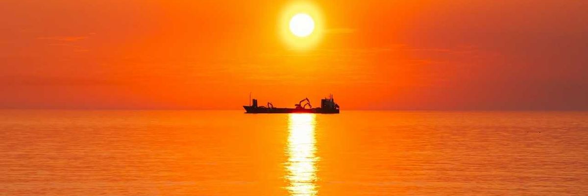 Boat on the ocean highlighted against an orange, burning sun