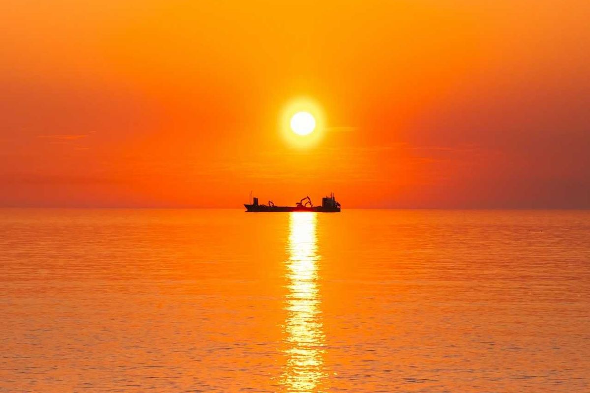 Boat on the ocean highlighted against an orange, burning sun