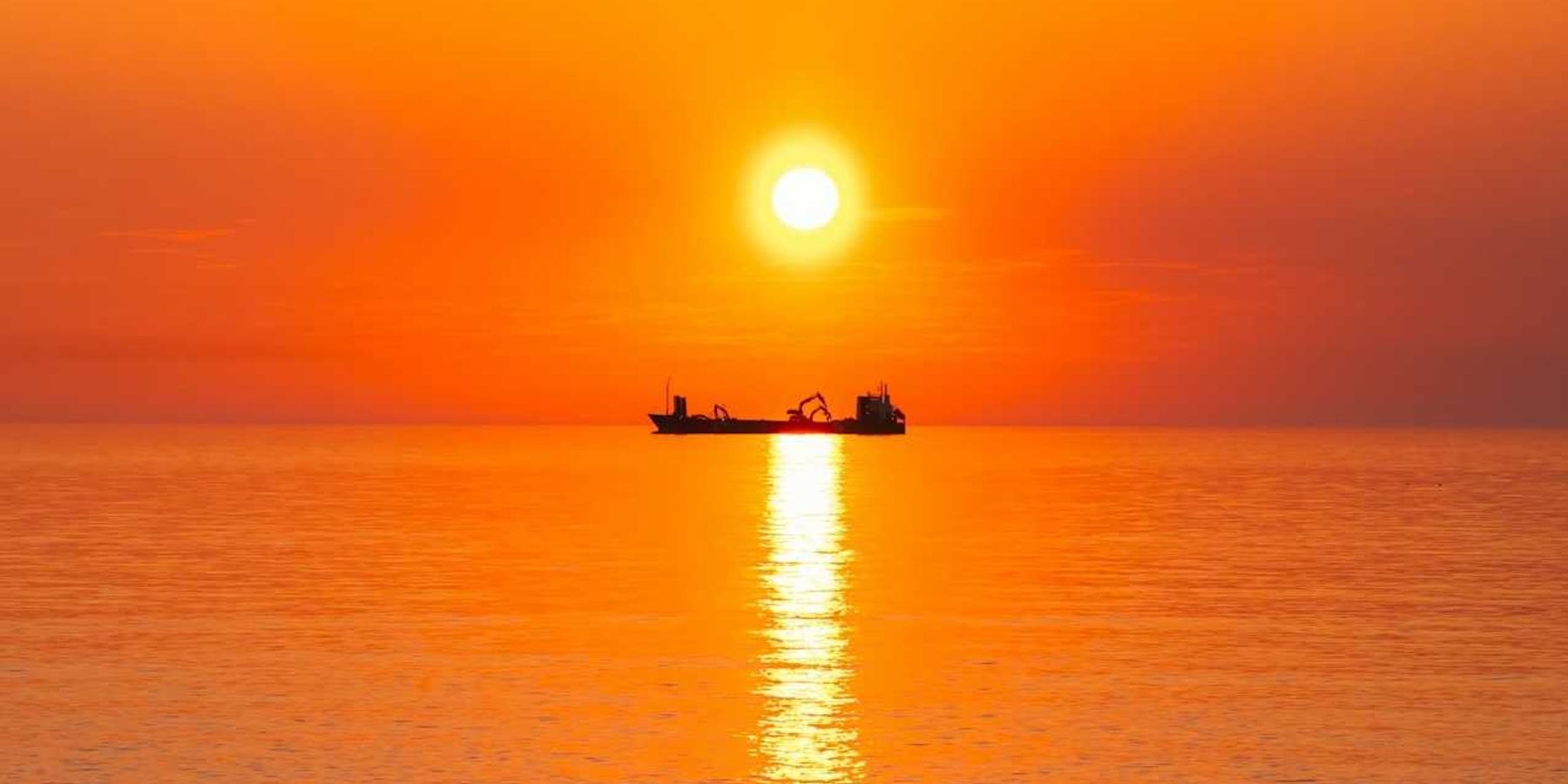 Boat on the ocean highlighted against an orange, burning sun