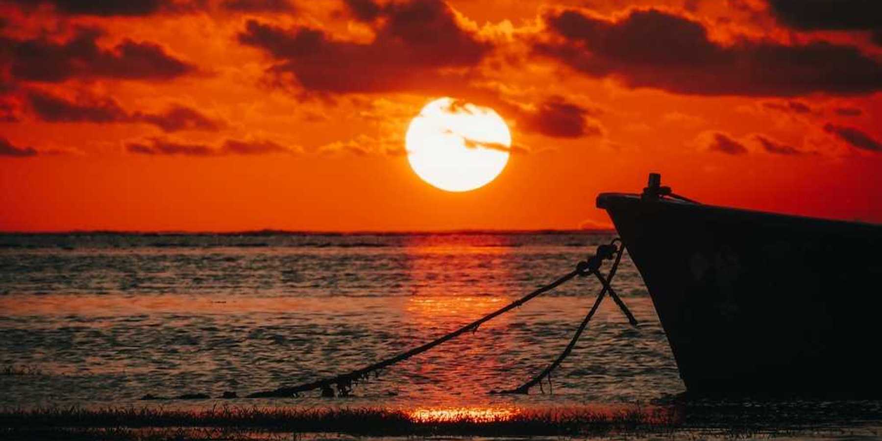 Bow of a moored boat against a brilliant red-orange sunset over the ocean