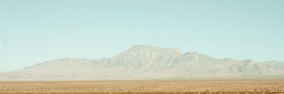 brown field near mountain under blue sky during daytime