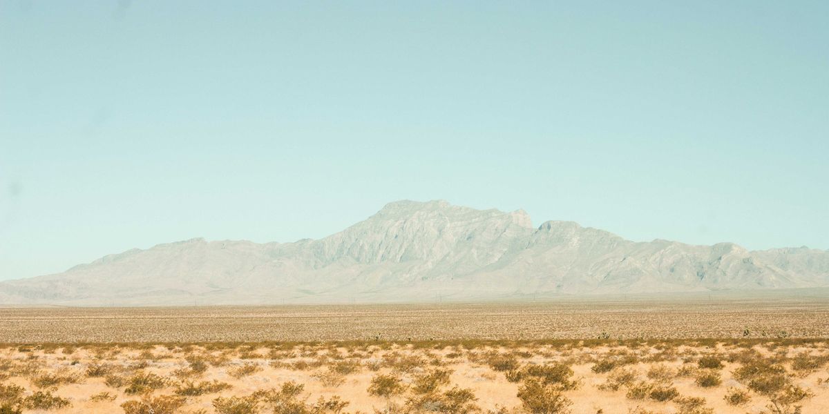 brown field near mountain under blue sky during daytime