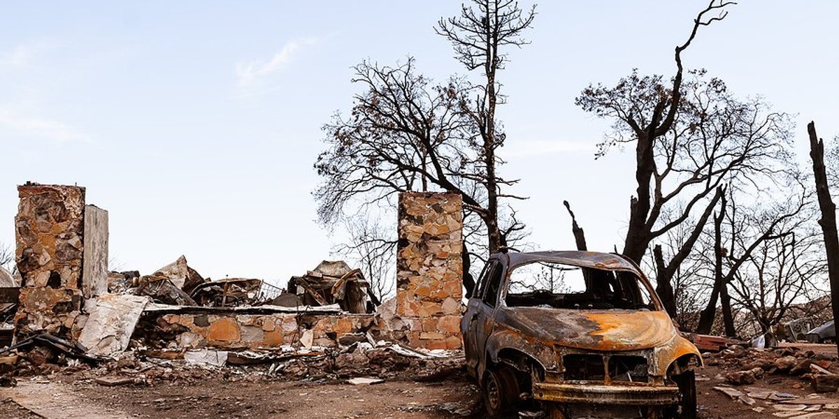 Burned foundation of a home next to burned out car and trees.