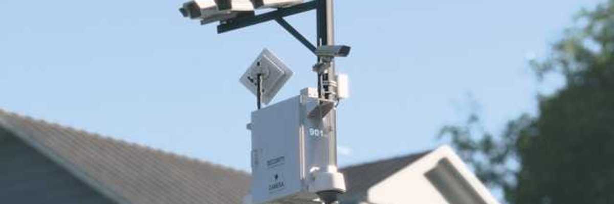 Cameras mounted on a tall pole with a house in the background