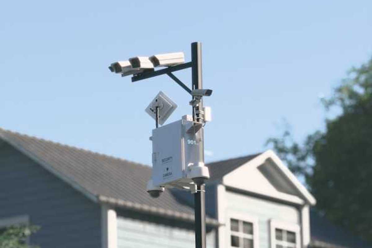 Cameras mounted on a tall pole with a house in the background