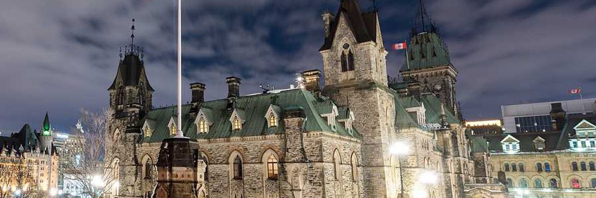 Canadian parliament building with a Canadian flag waving above it on a dark night