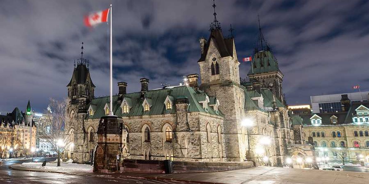 Canadian parliament building with a Canadian flag waving above it on a dark night