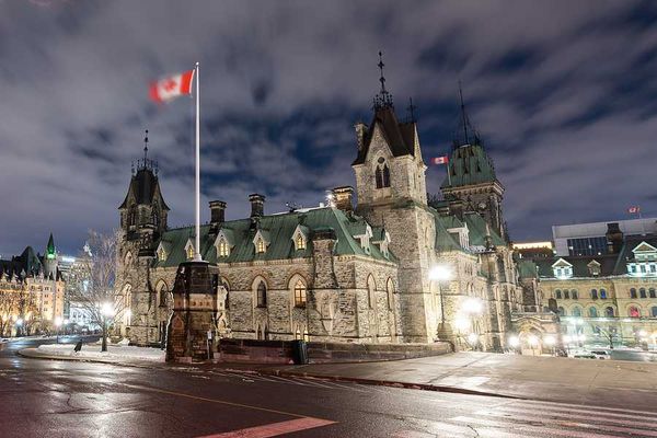 Canadian parliament building with a Canadian flag waving above it on a dark night