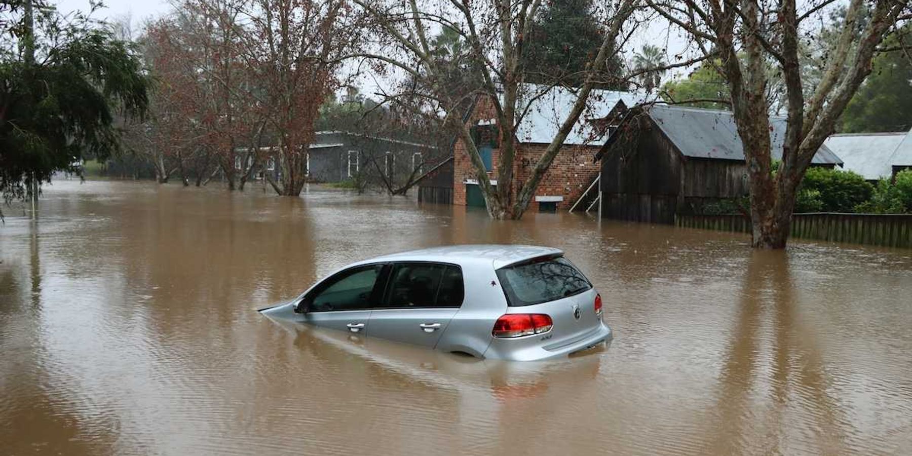 Car bobbing in brown floodwaters on flooded street in flooded neighborhood