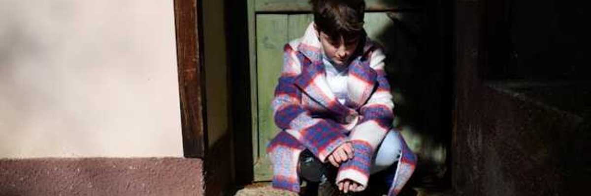 Child sitting in a doorway and looking down at the ground