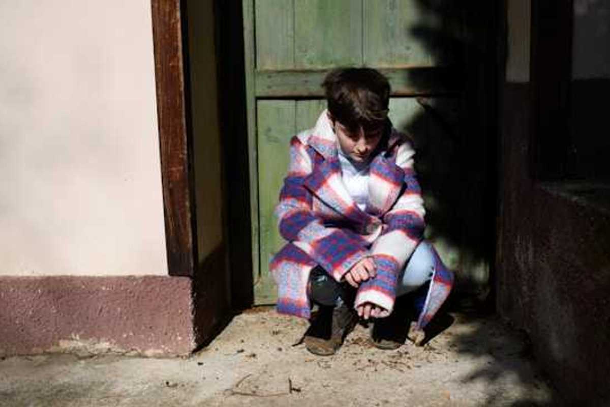 Child sitting in a doorway and looking down at the ground