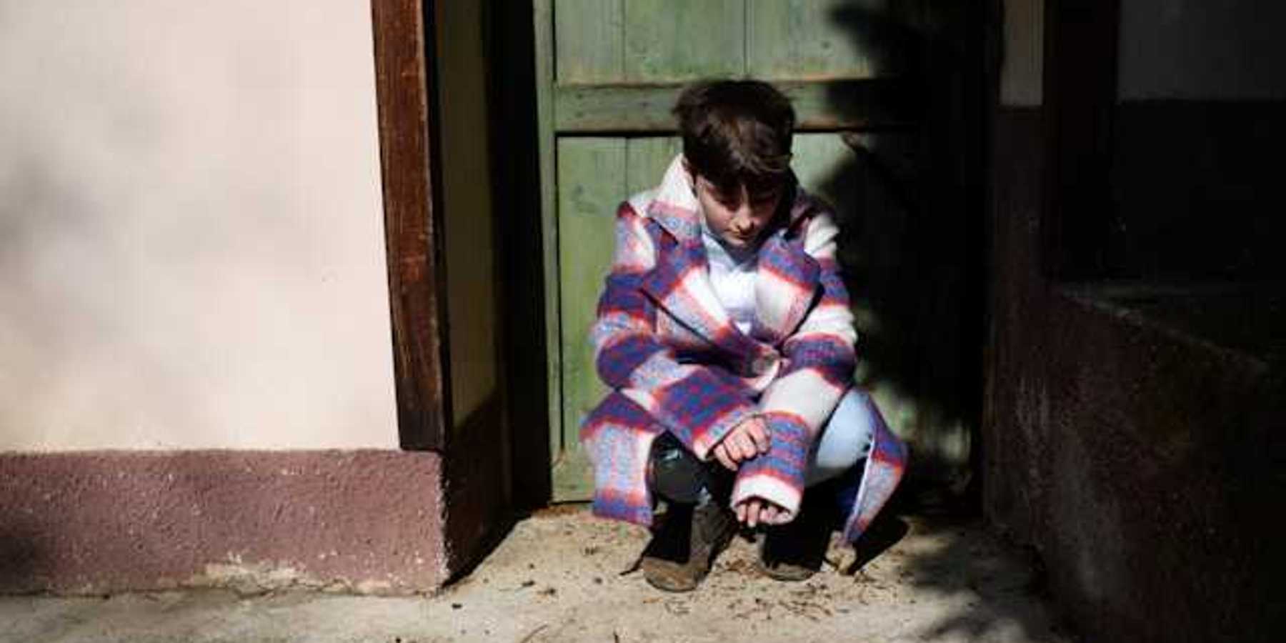 Child sitting in a doorway and looking down at the ground