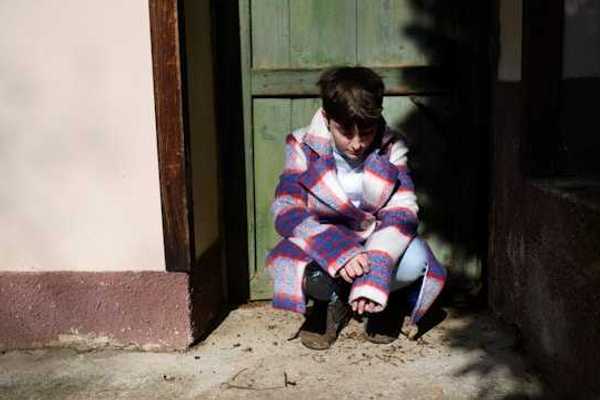 Child sitting in a doorway and looking down at the ground