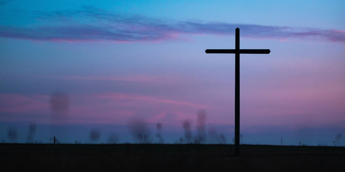 Christian cross standing under purple and blue evening sky.