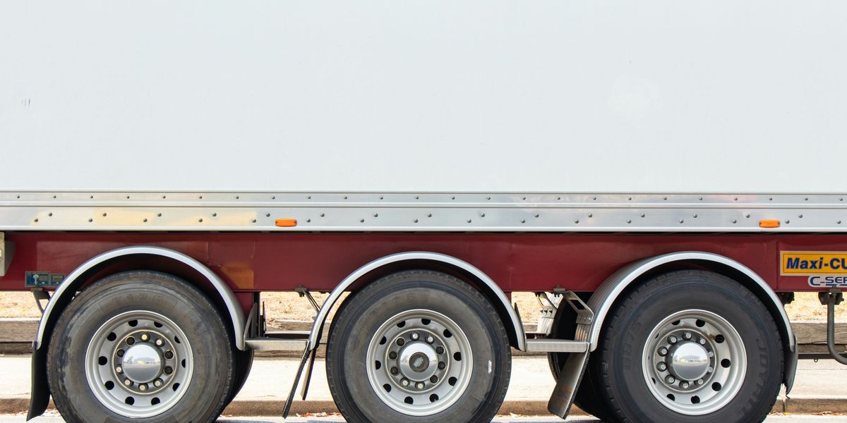 Closeup of the side of a flatbed truck showing three tires on one side.