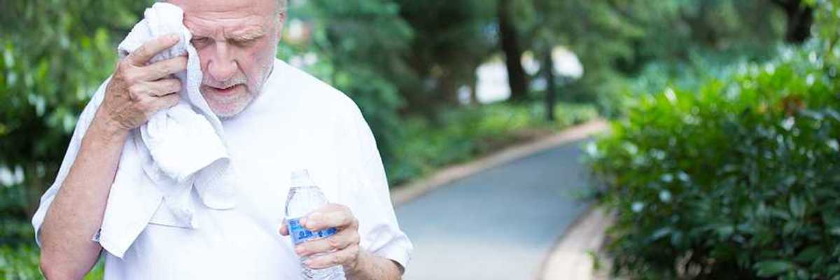 Closeup portrait old gentleman in white shirt having difficulties with extreme heat high temperature wiping sweat from face very tired isolated green trees paved road background