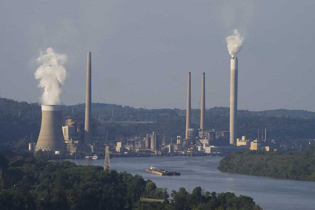 Coal fired electricity power plant along a river with a barge loaded with coal in the foreground.