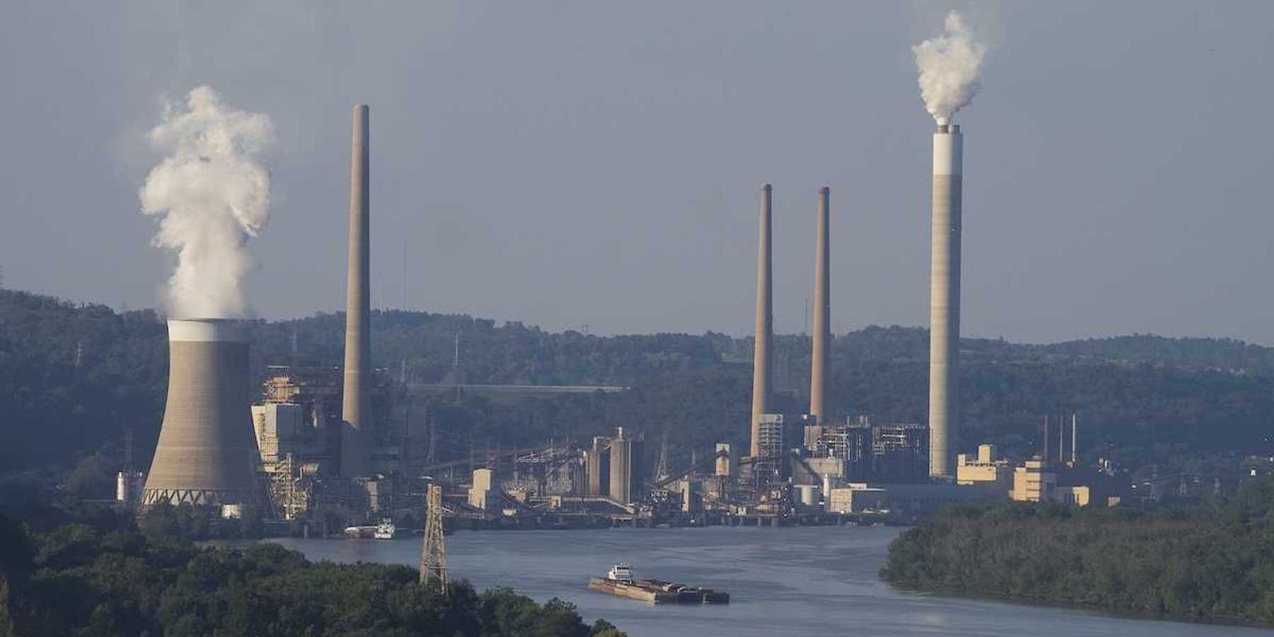 Coal fired electricity power plant along a river with a barge loaded with coal in the foreground.