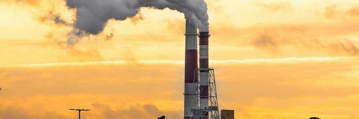 Coal fired power plant with two red/white smokestacks rising above a huge pile of coal, awaiting burning