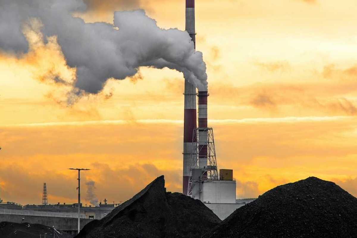 Coal fired power plant with two red/white smokestacks rising above a huge pile of coal, awaiting burning