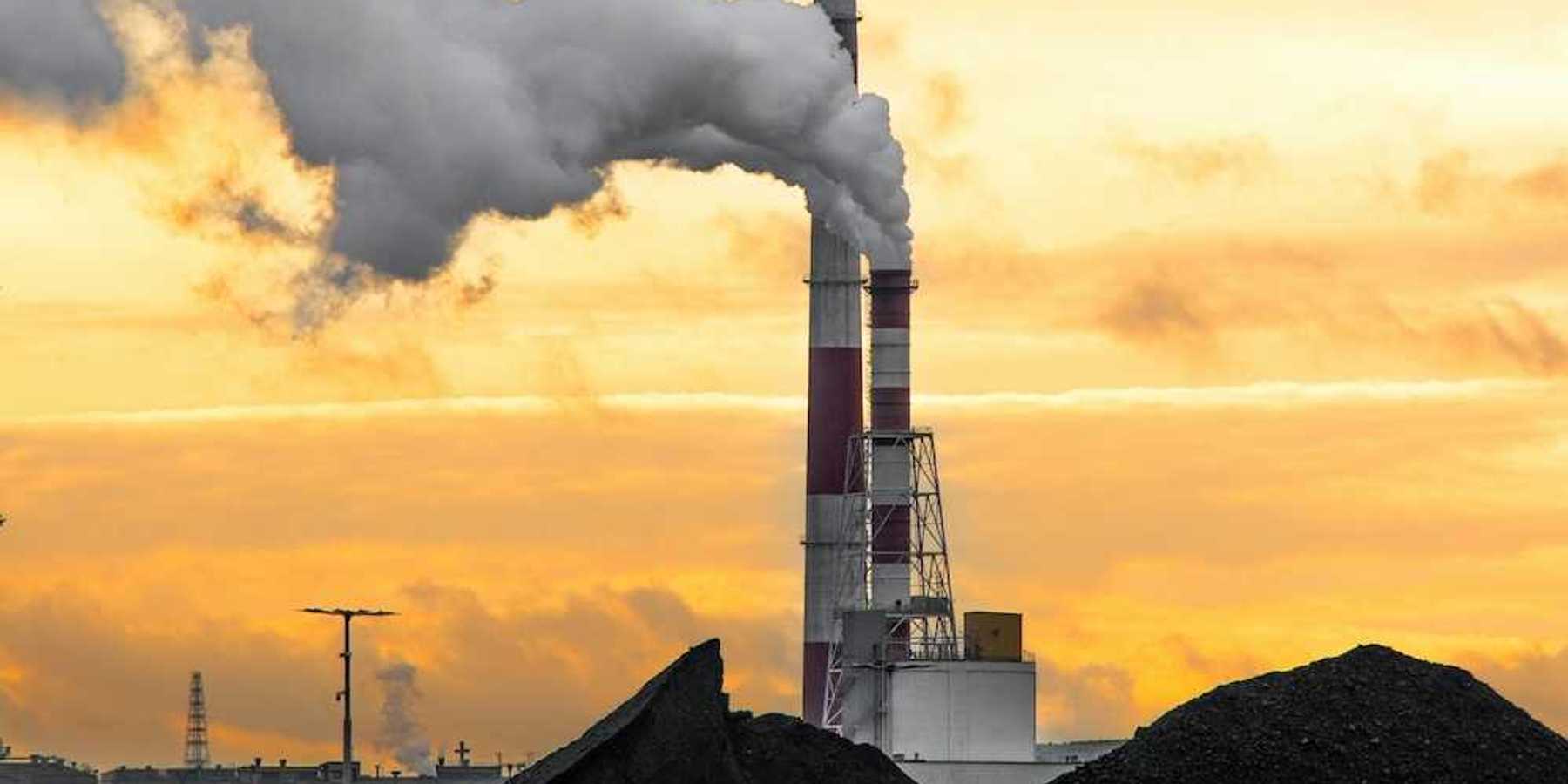 Coal fired power plant with two red/white smokestacks rising above a huge pile of coal, awaiting burning