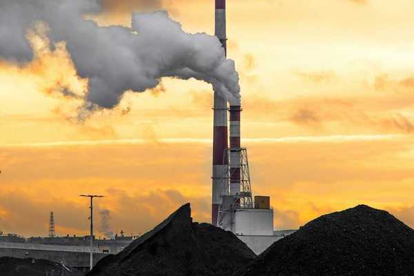 Coal fired power plant with two red/white smokestacks rising above a huge pile of coal, awaiting burning