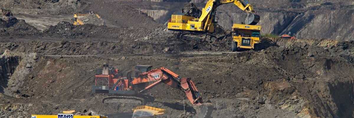 Coal mining operation featuring yellow rock trucks and excavators as well as one orange excavator in the center.