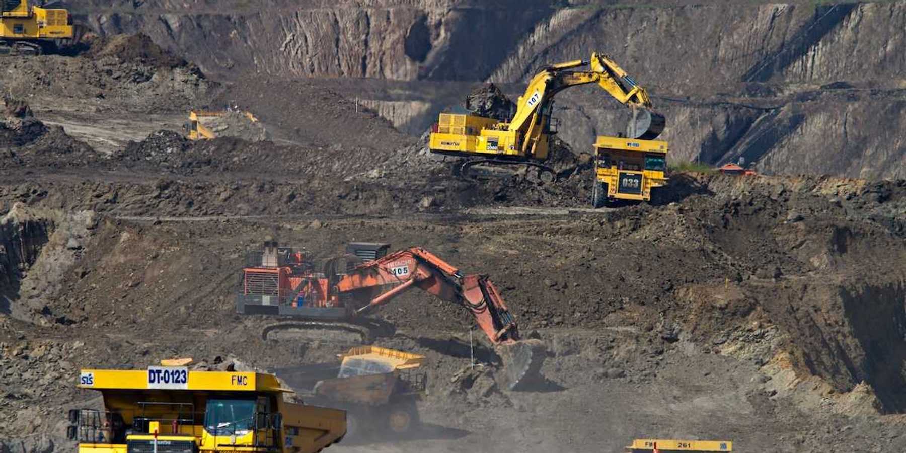 Coal mining operation featuring yellow rock trucks and excavators as well as one orange excavator in the center.