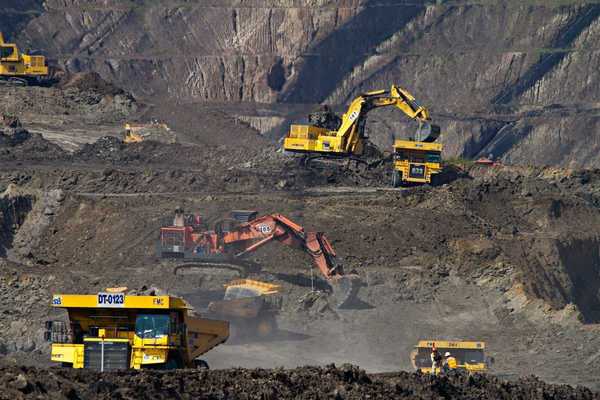 Coal mining operation featuring yellow rock trucks and excavators as well as one orange excavator in the center.