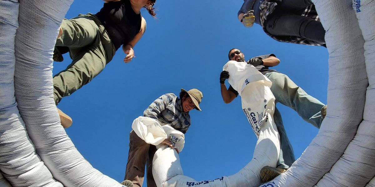 Coils of dirt-filled white tubs being stacked by workers to form a home.