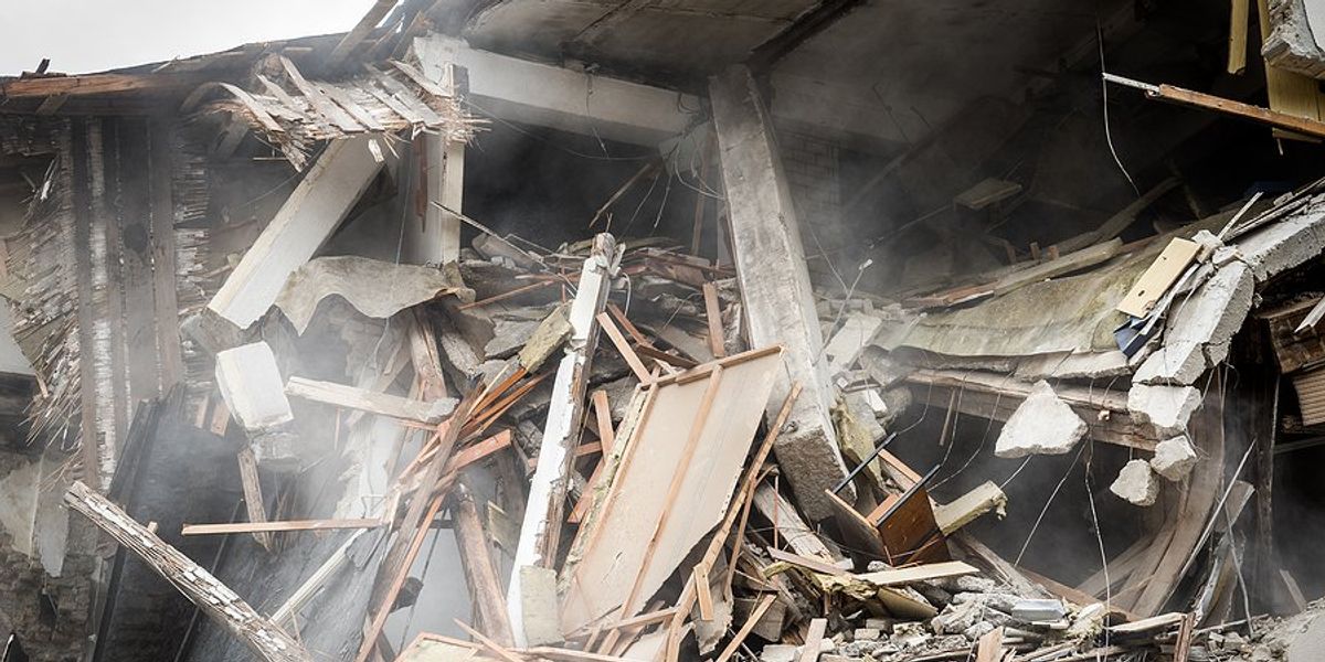 Collapsed house surrounded by rubble and wood debris.