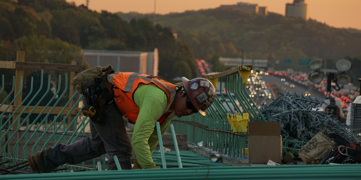 Construction worker on green galvanized iron sheet holding green bar.