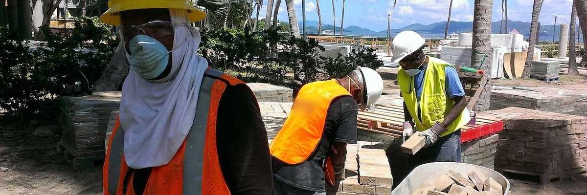 Construction workers move bricks on a tropical beach shoreline job site.