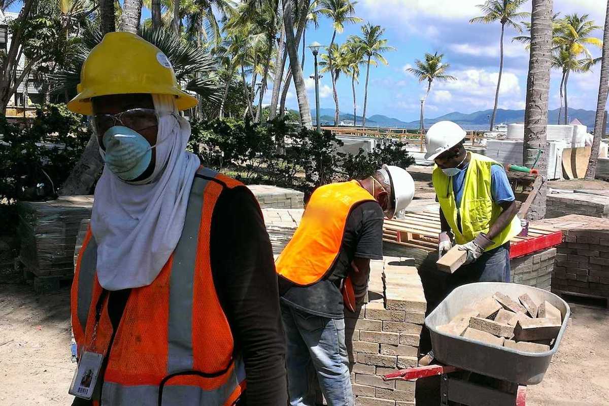 Construction workers move bricks on a tropical beach shoreline job site.