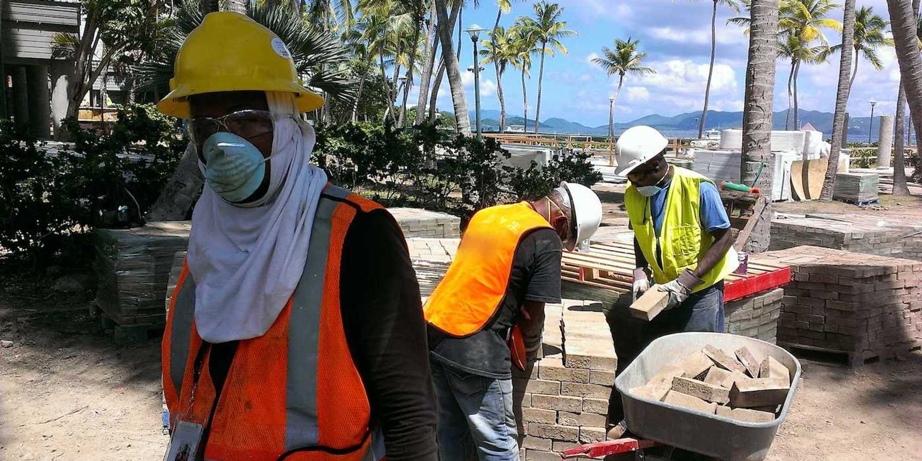 Construction workers move bricks on a tropical beach shoreline job site.