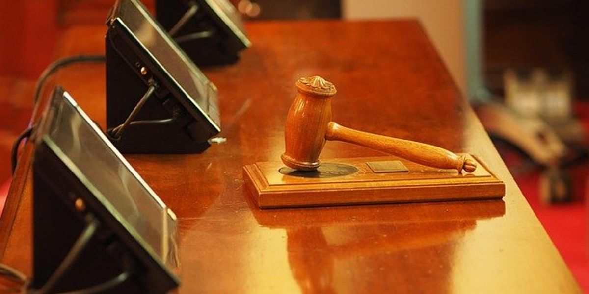Court gavel on a table in front of three small screens.