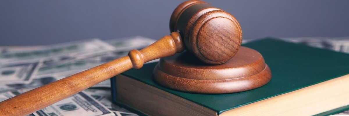 Court gavel resting on unnamed book which is sitting on scattered $100 bills.