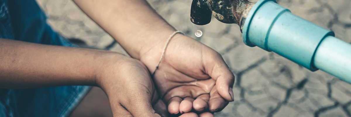 Cupped child-hands catching drops of water from a tap above cracked, dry earth