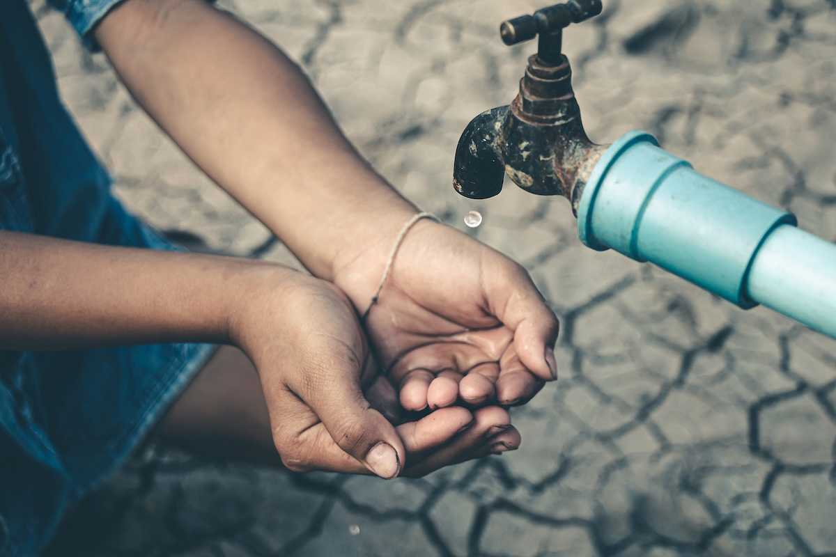 Cupped child-hands catching drops of water from a tap above cracked, dry earth