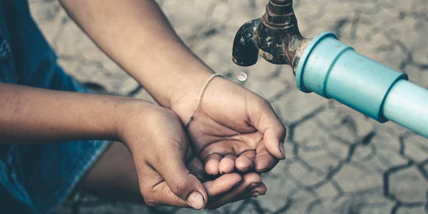 Cupped child-hands catching drops of water from a tap above cracked, dry earth
