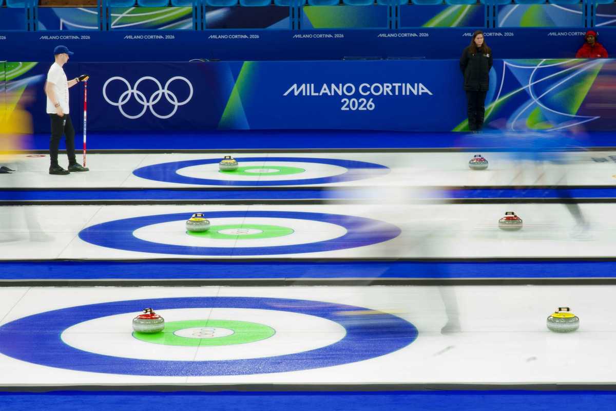 Curling match at Cortina Winter Olympics 2026 with athletes sliding stones on ice and fans in stands behind.