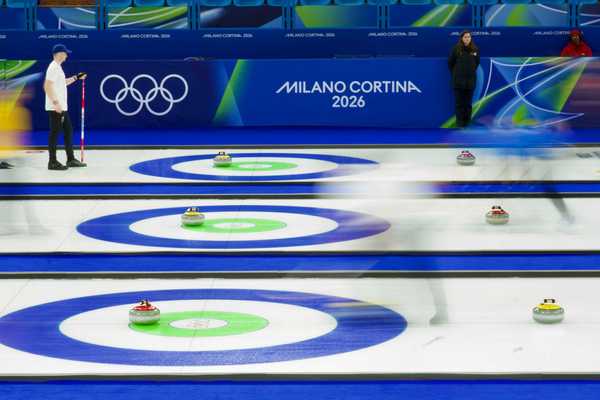 Curling match at Cortina Winter Olympics 2026 with athletes sliding stones on ice and fans in stands behind.
